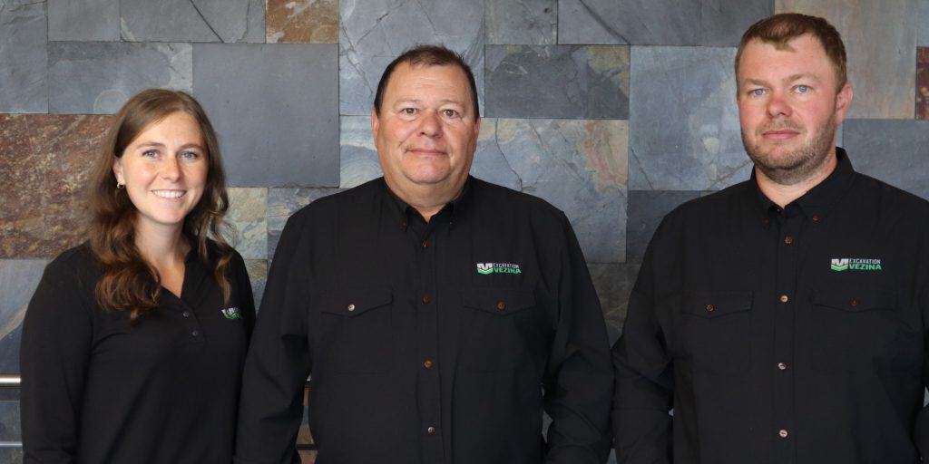 Trois professionnels souriants portant des uniformes noirs devant un mur en pierre.