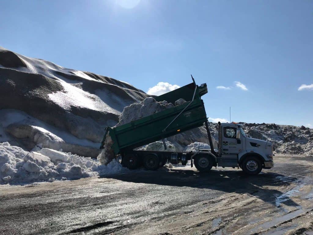 Camion déchargeant de la neige sur une route enneigée en montagne.