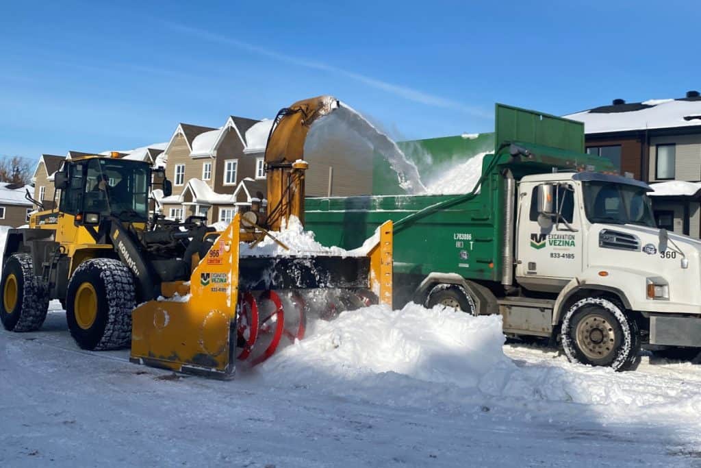 Équipement de déneigement commercial en action avec une pelle mécanique et un camion.