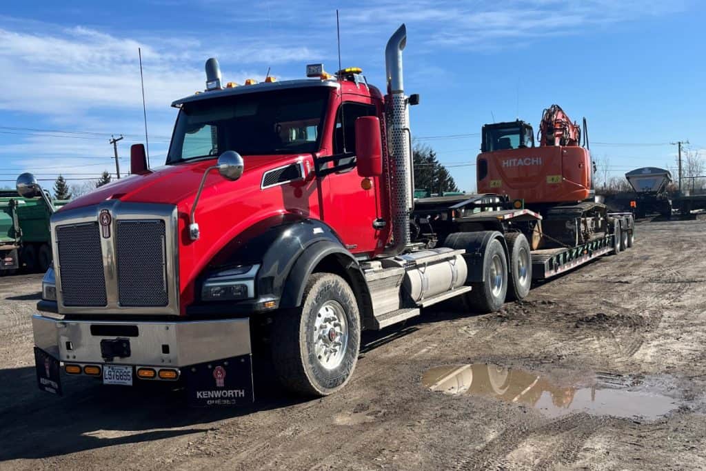 Camion de transport de machinerie lourde rouge avec excavatrice Hitachi.